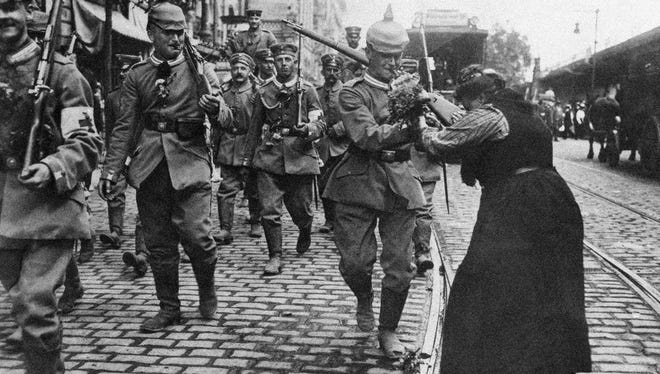 Girls and women throw flowers to Prussian guard infantry in new field gray uniforms as they leave Berlin, Germany, to  train for the front in August 1914 during World War I.