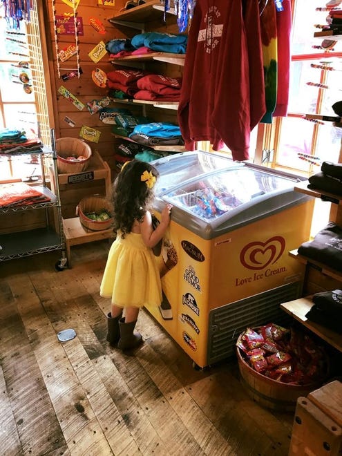 Daughter Ellie, in her summer dress and rubber boots, looks over her ice cream choices on a hot afternoon in July in "Summers in Glen Arbor," by Kylie Harig of Ferndale.