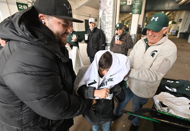 Dan and Joe Smith help son and grandson Joseph Smith, 7, center into Spartan football gear before the Michigan State football's spring showcase/scrimmage at Spartan Stadium.