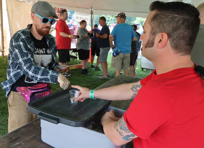 Kyle Kipp, 41, of Ypsilanti, hands a sample cup and tokens to a beer festival attendee Friday. Kipp said he lives in the neighborhood volunteers every year.