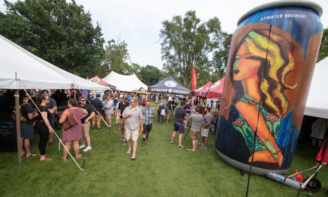 Visitors to the 2019 Michigan Brewers Guild Summer Beer Festival in Ypsilanti's Riverside Park walk between brewer tents and past a large Atwater Brewing inflatable beer can Friday.