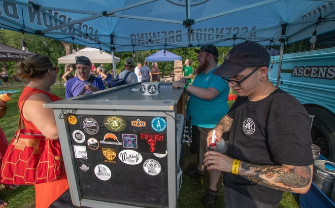 David Murphy, a brewer at Ascension Brewing, of Novi, uses a spray bottle to clean the glass of an attendee of the Michigan Brewers Guild 2019 Summer Beer Festival Friday.