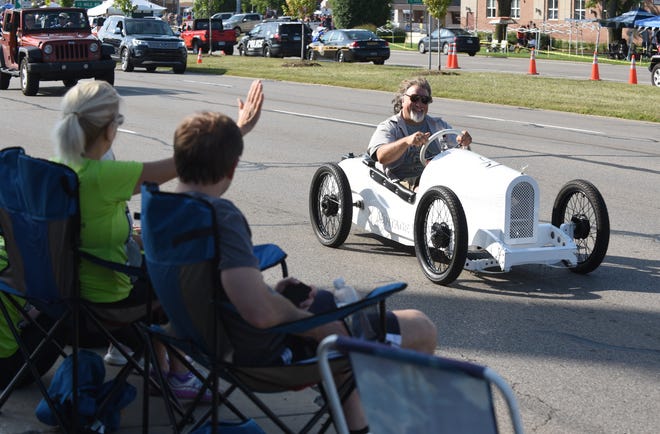 People wave at  a go-kart sized car making its way along Woodward near 13 Mile in Royal Oak.