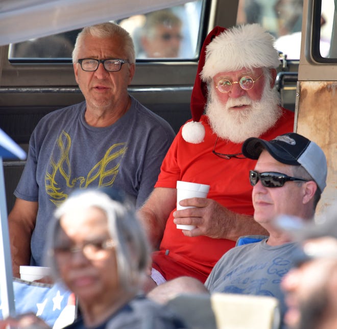 Dave Harrelson, left, of Arkansas, and Adam Lacy, right, of Rochester Hills, sit in the shade with Santa Claus, aka Tommy Roberts, center, of Philadelphia, Pa.