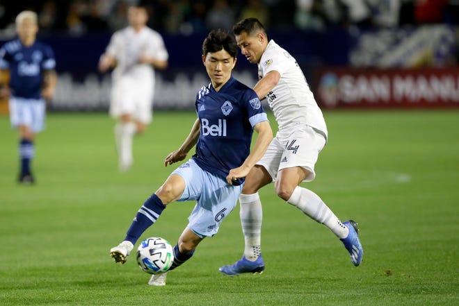 Vancouver Whitecaps midfielder Hwang In-Beom, left, controls the ball away from LA Galaxy forward Javier Hernandez, right, during a match March 7.