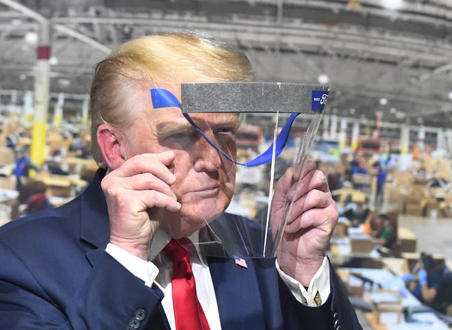 President Trump looks through a face shield, in front of poster of the manufacturing of these shields during a tour of the Ford Motor Company Rawsonville Components Plant, one of the many repurposed American factories producing personal protective equipment and ventilators in the fight against the COVID-19 pandemic in Ypsilanti, Michigan on May 21, 2020.