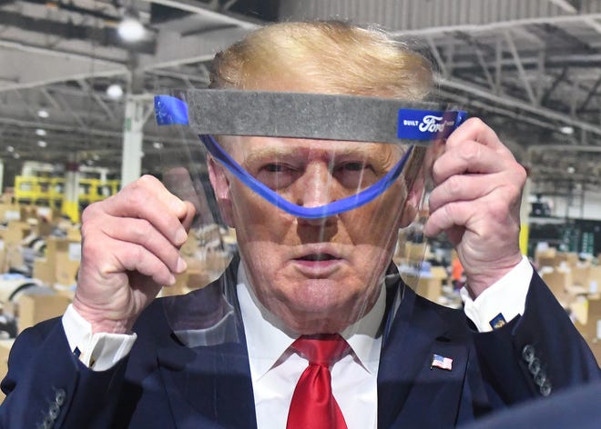 President Trump looks through a face shield, in front of poster of the manufacturing of these shields during a tour of the Ford Motor Company Rawsonville Components Plant, one of the many repurposed American factories producing personal protective equipment and ventilators in the fight against the COVID-19 pandemic in Ypsilanti, Michigan on May 21, 2020.