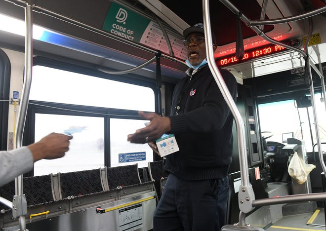 Bus driver Andrew Love hands a mask to a man who just got on the bus without one in Detroit on May 18, 2020.