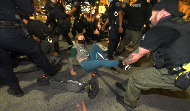 Police officers take people into custody as this officer pulls a woman out of the arrest zone. Protesters and police officers in riot gear clash on Randolph near Congress in downtown Detroit, Friday night, May 29, 2020, before a black male was shot by an unknown shooter on Congress behind the Checker Bar.