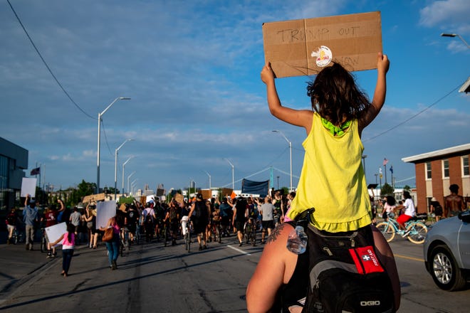 Mary Qutso, 4, of Dearborn holds a sign while on the shoulders of Riley Jane, 29, of Ferndale while marching toward the Detroit Police Department's 4th Precinct in Detroit on June 30, 2020.
