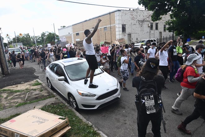 A protester stands on a parked car along San Juan Road and cheers as marchers head towards Woodward Avenue in Detroit on Saturday, July 11, 2020.