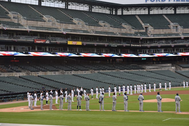 Tigers and Royals players stand during the national anthem.