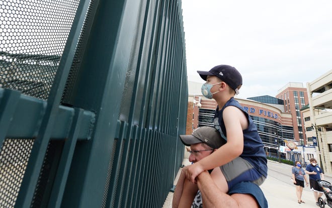 Benjamin Hamilton, 7, of Taylor sits on his father's Scott Hamilton's shoulders to watch the Tigers home opener against the Royals outside the fence at Comerica Park.