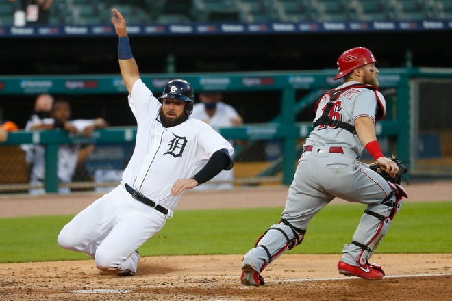 Detroit Tigers' Austin Romine slides safely into home plate as Cincinnati Reds catcher Tucker Barnhart (16) waits for the throw in the sixth inning of a baseball game in Detroit, Friday, July 31, 2020. (AP Photo/Paul Sancya)