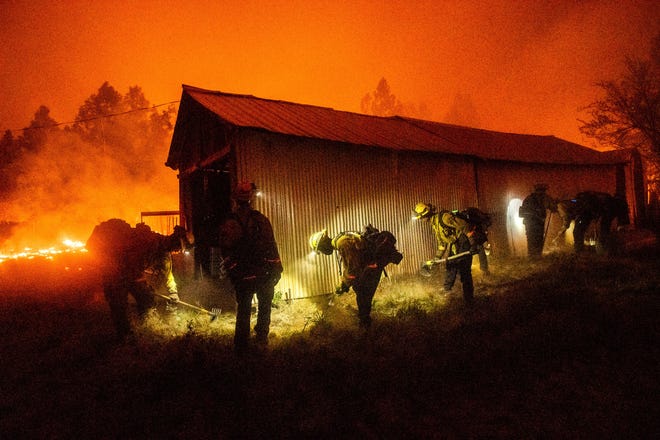 A hand crew clears vegetation from around a barn as the Bear Fire burns through the Berry Creek area of Butte County, Calif., on Wednesday, Sept. 9, 2020. The blaze, part of the lightning-sparked North Complex, expanded at a critical rate of spread as winds buffeted the region.
