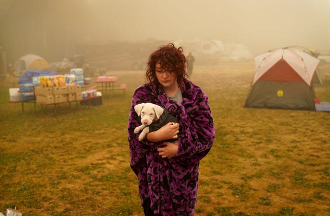 Shayanne Summers holds her dog Toph while wrapped in a blanket after several days of staying in a tent at an evacuation center at the Milwaukie-Portland Elks Lodge, Sunday, Sept. 13, 2020, in Oak Grove, Ore. "It's nice enough here you could almost think of this as camping and forget everything else, almost," said Summers about staying at the center after evacuating from near Molalla, Oregon which was threatened by the Riverside Fire.