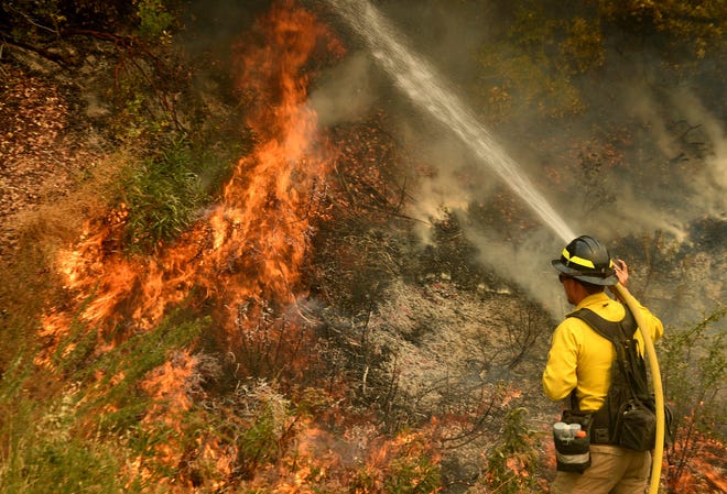 A firefighter puts out a hot spot along Highway 38 northwest of Forrest Falls, Calif., as the El Dorado Fire continues to burn Thursday afternoon, Sept. 10, 2020. The fire started by a device at a gender reveal party on Saturday.