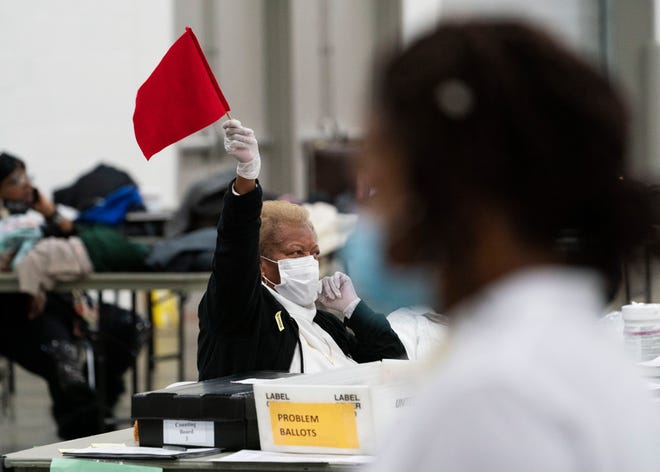 An election inspector waves a flag to call for assistance as ballots are counted into the early morning hours Wednesday, Nov. 4, 2020, at the central counting board in Detroit.