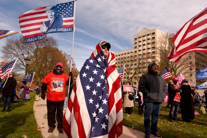 Michael Foy of Wixom wraps himself in the flag in the chill outside as President Donald Trump supporters gather at the state Capitol Building  in Lansing for a "Stop the Steal" rally disputing the presidential voting Saturday, October 14, 2020.
