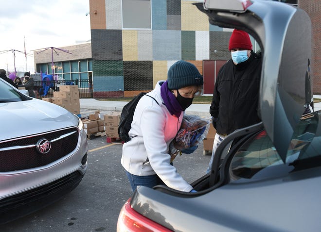 From left, Volunteers Renee VanderHagen, 56, of Macomb Township and Tony Rosales of Sterling Heights load food into a car at the Forgotten Harvest mobile food pantry at the Sterling Heights Community Center in Sterling Heights, Mich. on Jan. 7, 2021.