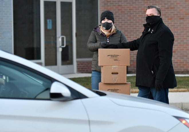 From left, Volunteer Rachel Lasater stacks boxes while her husband and fellow volunteer Ted Lasater, 52, of Macomb pause from putting food in cars at the Forgotten Harvest mobile food pantry at the Sterling Heights Community Center in Sterling Heights, Mich. on Jan. 7, 2021.