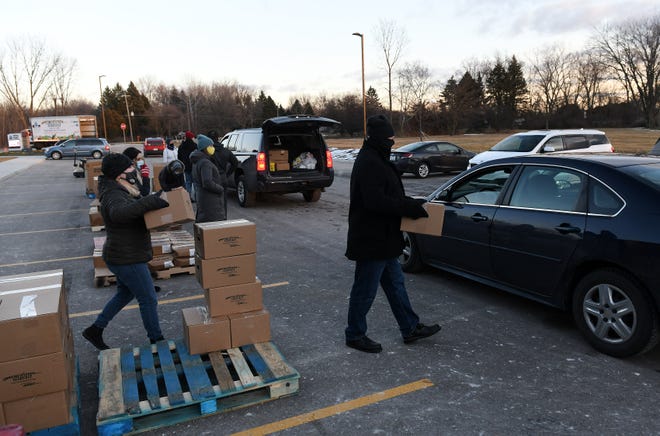 From left, Volunteer Rachel Lasater stacks boxes while her husband and fellow volunteer Ted Lasater, 52, of Macomb carries a box of food to a car at the Forgotten Harvest mobile food pantry at the Sterling Heights Community Center in Sterling Heights, Mich. on Jan. 7, 2021.