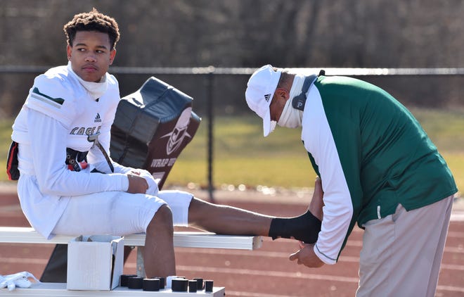Cass Tech head coach Thomas Wilcher tapes the ankles of Jameel Gardner (9) minutes before the start of the game as Belleville hosts Detroit Cass Tech during an MHSAA Division 1 regional final, Saturday afternoon, Jan. 9, 2021.