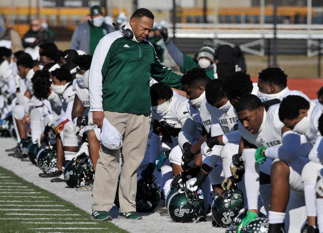 Cass Tech head coach Thomas Wilcher stands as his team kneels during the national anthem.