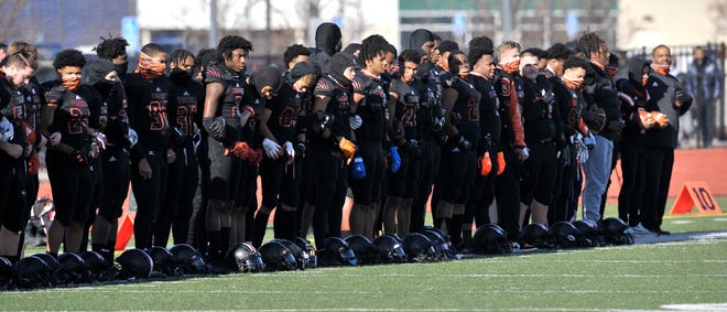 Member of the Belleville football team interlock arms as they stand for the national anthem.