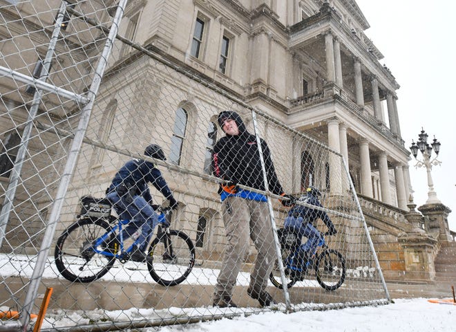 Dakota Pitz, of National Construction Rentals, puts up fencing, as Michigan State Police officer patrol on bicycle, around the Michigan State Capitol in preparation for possible protests over the weekend in Lansing, Michigan.
