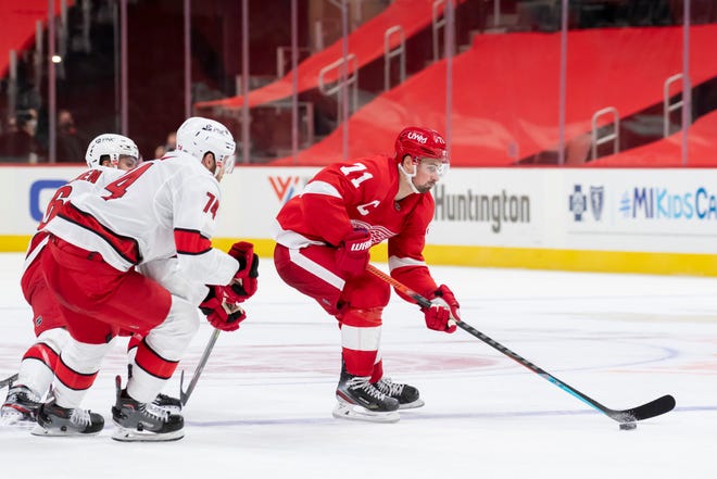 Detroit center Dylan Larkin keeps the puck away from Carolina left wing Teuvo Teravainen, left, and defenseman Jaccob Slavin in the third period during a game between the Detroit Red Wings and the Carolina Hurricanes, at Little Caesars Arena, in Detroit, January 14, 2021.