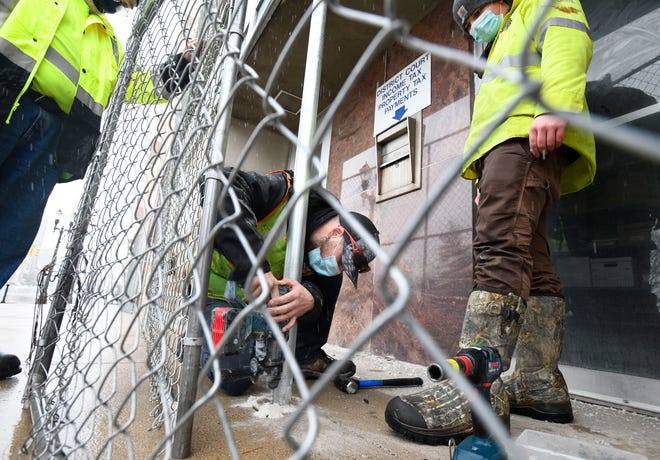 Travis Smith and Austen Tews, of Pro-Soil Site Services Inc., drill holes into the cement while putting up emergency exit fencing barricades at Lansing City Hall in preparation for possible protests at the capital over the weekend, in Lansing, Michigan.