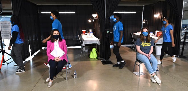 Several Protect Michigan Commission COVID-19 student ambassador volunteers walk behind Gov. Gretchen Whitmer, seated left, and her daughter, Sherry Shrewsbury, seated right, before everyone receives their COVID-19 vaccinations at Ford Field, Tuesday morning, April 6, 2021.