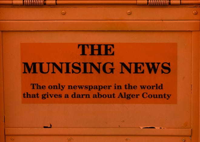 Included above The Munising News banner in print and on the front of the orange newspaper vending boxes, like this one show on Tuesday, March 30, 2021, are these words: "The Munising News, The only newspaper in the world that gives a darn about Alger County."