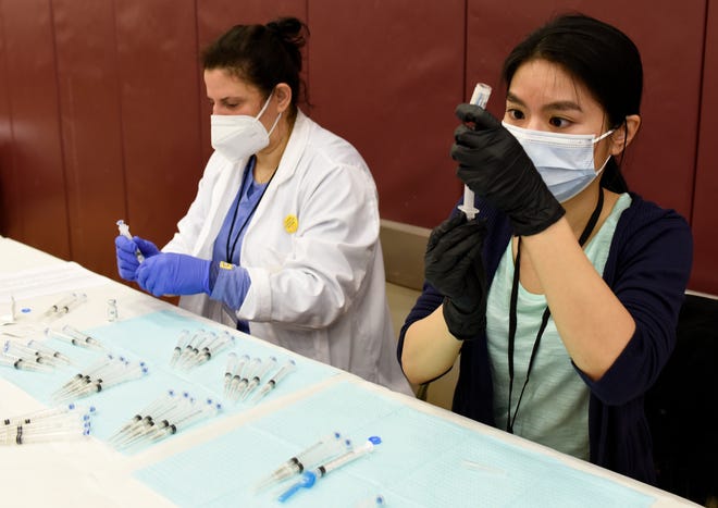 Pharmacists Nabilah Seblini, left, and Julie Nguyen fill syringes with the Johnson & Johnson vaccine during a vaccination clinic at Western International High School.