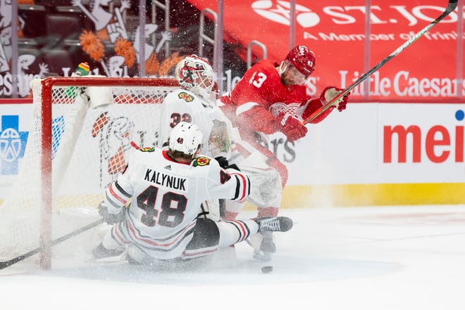 Chicago defenseman Wyatt Kalynuk collides into teammate goaltender Kevin Lankinen while battling for the puck with Detroit left wing Darren Helm in the third period during a game between the Detroit Red Wings and the Chicago Blackhawks, at Little Caesars Arena, in Detroit, April 15, 2021.