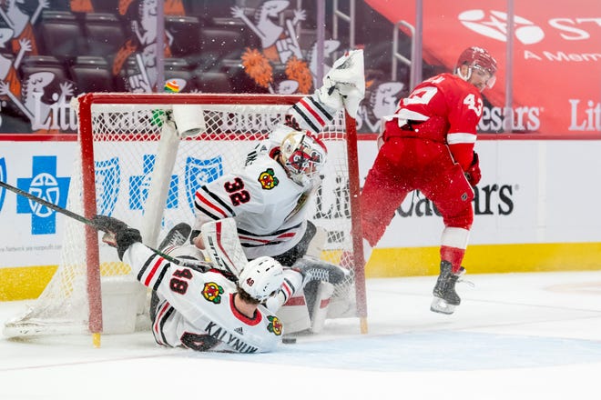 Chicago defenseman Wyatt Kalynuk collides into teammate goaltender Kevin Lankinen while battling for the puck with Detroit left wing Darren Helm in the third period during a game between the Detroit Red Wings and the Chicago Blackhawks, at Little Caesars Arena, in Detroit, April 15, 2021.