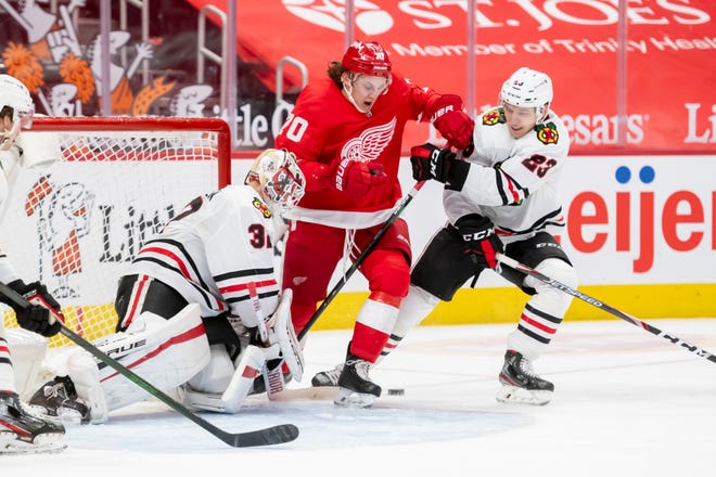 Detroit defenseman Troy Stecher battles for the puck with Chicago goaltender Kevin Lankinen, left, and Chicago left wing Philipp Kurashev in the third period during a game between the Detroit Red Wings and the Chicago Blackhawks, at Little Caesars Arena, in Detroit, April 15, 2021.