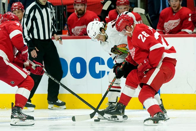 Detroit Red Wings left wing Adam Erne (73), Red Wings defenseman Gustav Lindstrom (28) and Chicago Blackhawks left wing Alex DeBrincat (12) reach for the puck during the third period of an NHL hockey game, Saturday, April 17, 2021, in Detroit.