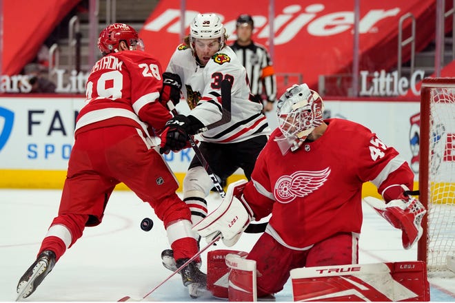 Detroit Red Wings goaltender Jonathan Bernier, right, deflects a shot as Red Wings defenseman Gustav Lindstrom (28) checks Chicago Blackhawks left wing Brandon Hagel (38) during the first period of an NHL hockey game, Saturday, April 17, 2021, in Detroit.