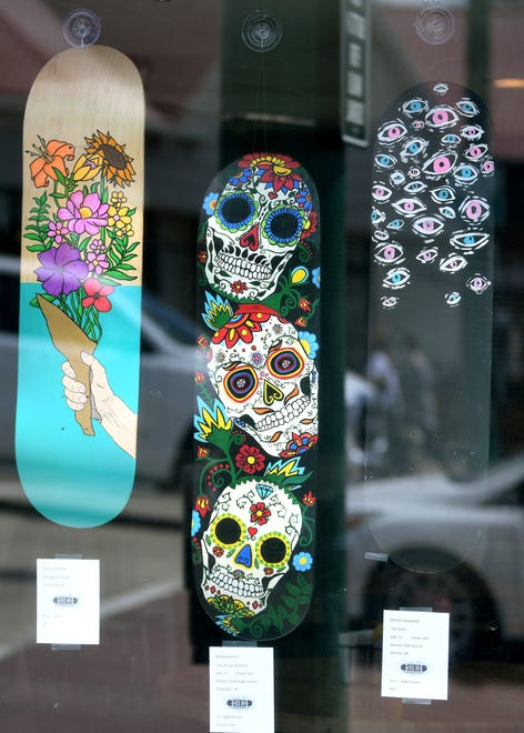 Deck Art 2021 adult category entry "Flower Bouquet" by Devin Frazier of Ortonville, Stoney Creek High School student Olivia Ambro, 14 entry titled "Dia De Los Muertos," and Almont High School student Alexis Campbell her entry "All Eyes" fill the window at Chomp restaurant in downtown Rochester.
