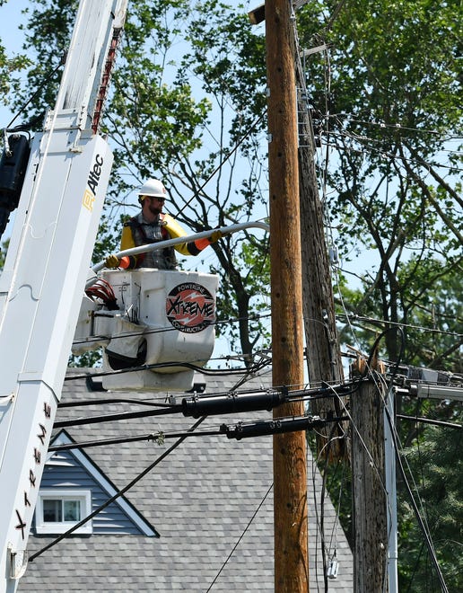 A worker from Xtreme Powerline Construction works to restore power where a new pole has been installed near North Fulton Street.  A mix of volunteers and work crews clean up the area after Saturday's tornado in Armada, Michigan, on July 26, 2021.