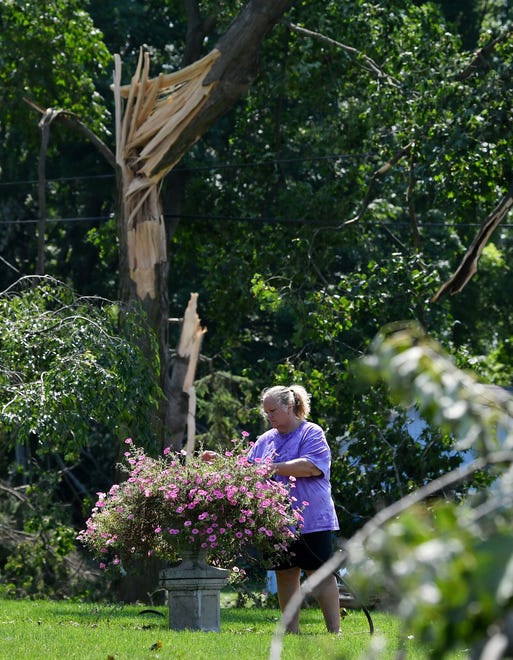 Angela Cunningham waters her petunias at her home on West Main Street. A mix of volunteers and work crews clean up after Saturday's tornado in Armada, Michigan, on July 26, 2021.