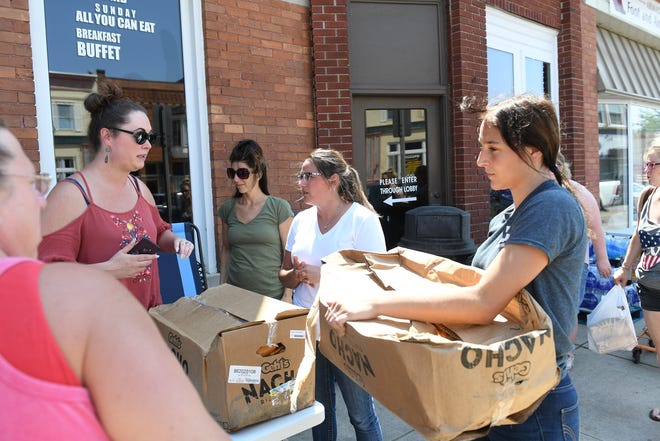 Kristin Rakos, 38, of Armada Township, left, receives food donations from Tiffany Warbington, in white, and Megan Vissotski from Vinckier Foods. Rakos is helping to organize one of the volunteer operations to get food and water to people affected by the storm or involved with the clean up effort. A mix of volunteers and work crews clean up the area after Saturday's tornado in Armada, Michigan, on July 26, 2021.