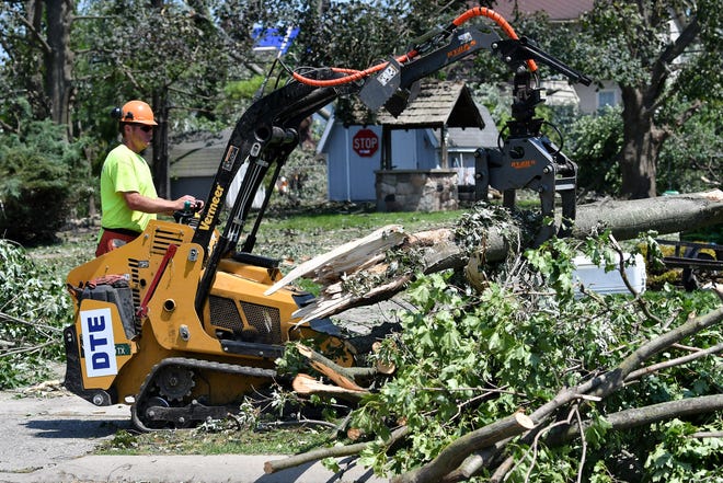 A worker moves part of a tree into a pile to be removed or mulched. A mix of volunteers and work crews clean up the area after Saturday's tornado in Armada, Michigan, on July 26, 2021.