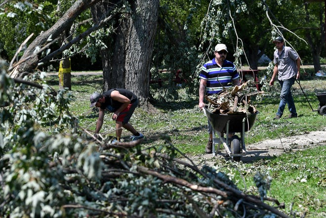 Juan Martinez, 47, center, of Mount Clemens wheels a load of branches toward a pile at the Village of Armada Memorial Park. A mix of volunteers and work crews clean up the area after Saturday's tornado in Armada, Michigan, on July 26, 2021.