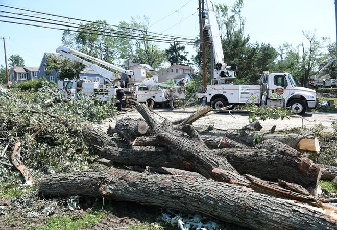Large pieces of trees that came down in the Village of Armada Memorial Park are piled as crews from Xtreme Powerline Construction work to restore power where a new pole has been installed near North Fulton Street.  A mix of volunteers and work crews clean up the area after Saturday's tornado in Armada, Michigan, on July 26, 2021.