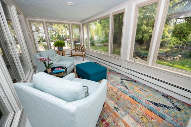 The spacious sunroom has plenty of windows overlooking the pond. A sitting area on one side features a pair of chairs in a soothing aqua blue fabric and a colorful rug.