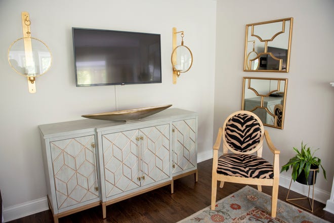A zebra print chair sits below a pair of decorative mirrors that were a recent purchase. Decorative sconces flank the TV above a console.