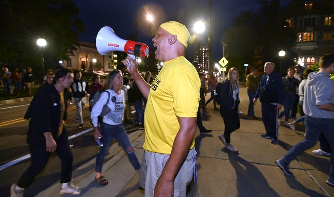 Anderson sexual-assault survivor Chuck Christian yells on the bull horn as he, fellow survivors and supporters prepare to pose for a picture in front of the Lawyer's Club and Munger Residences building, Wednesday night, October 13, 2021.